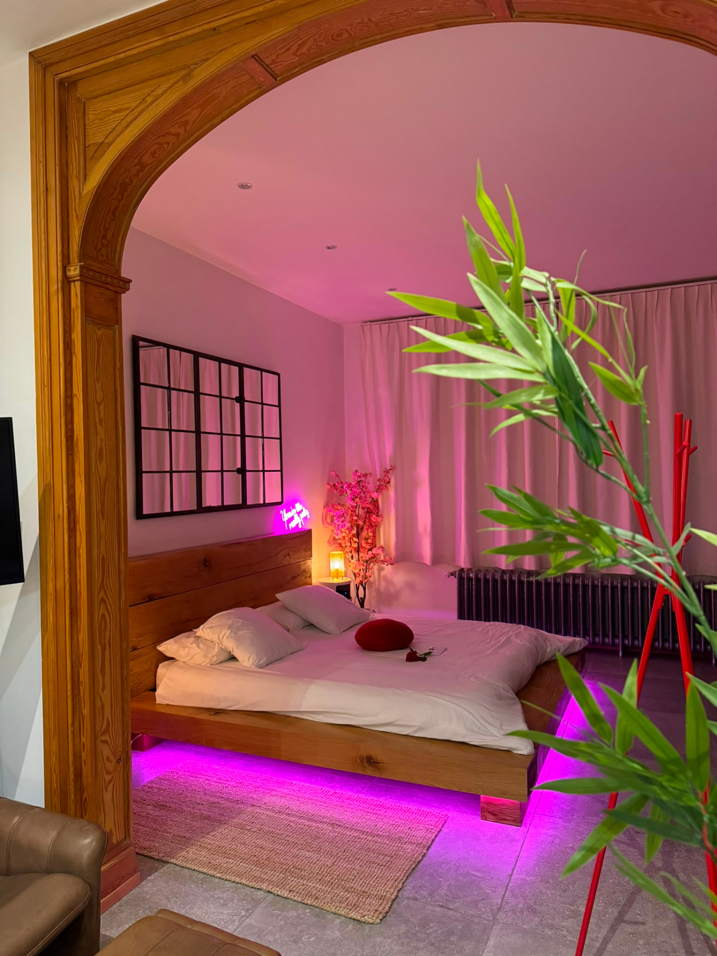 Chambre de L'Exotic Chimay, lit en bois sous une arche et éclairage rose